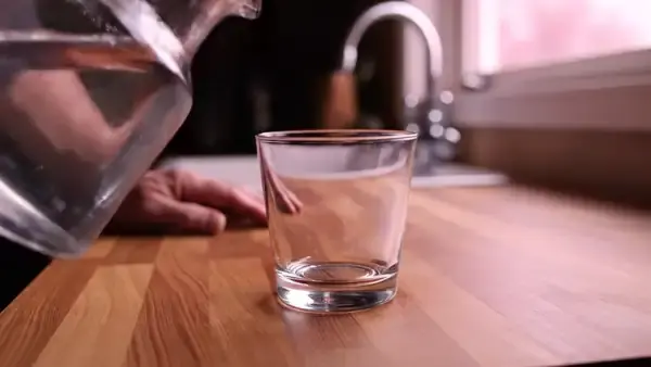 Water poured from a glass pitcher into a short drinking glass on a kitchen counter at dawn