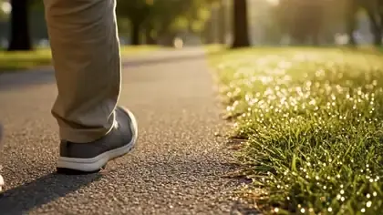 The feet of an older man in grey walking shoes passing along a park path at sunrise